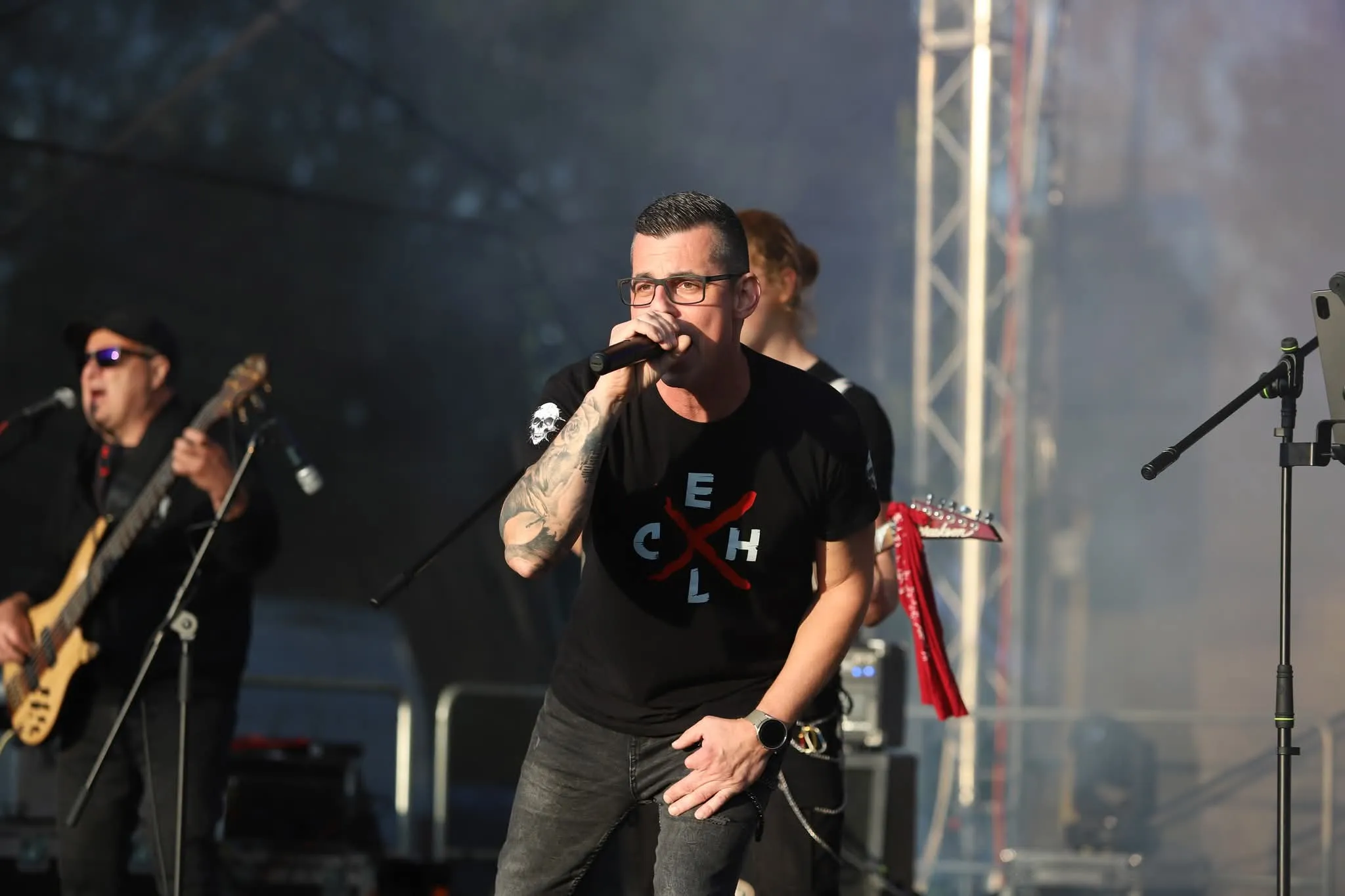 Zpěvák v tričku s monogramem kapely zpívá v kouři